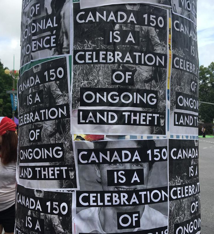 A telephone pole covered with handbills reading “Canada 150 is a celebration of ongoing land theft.”