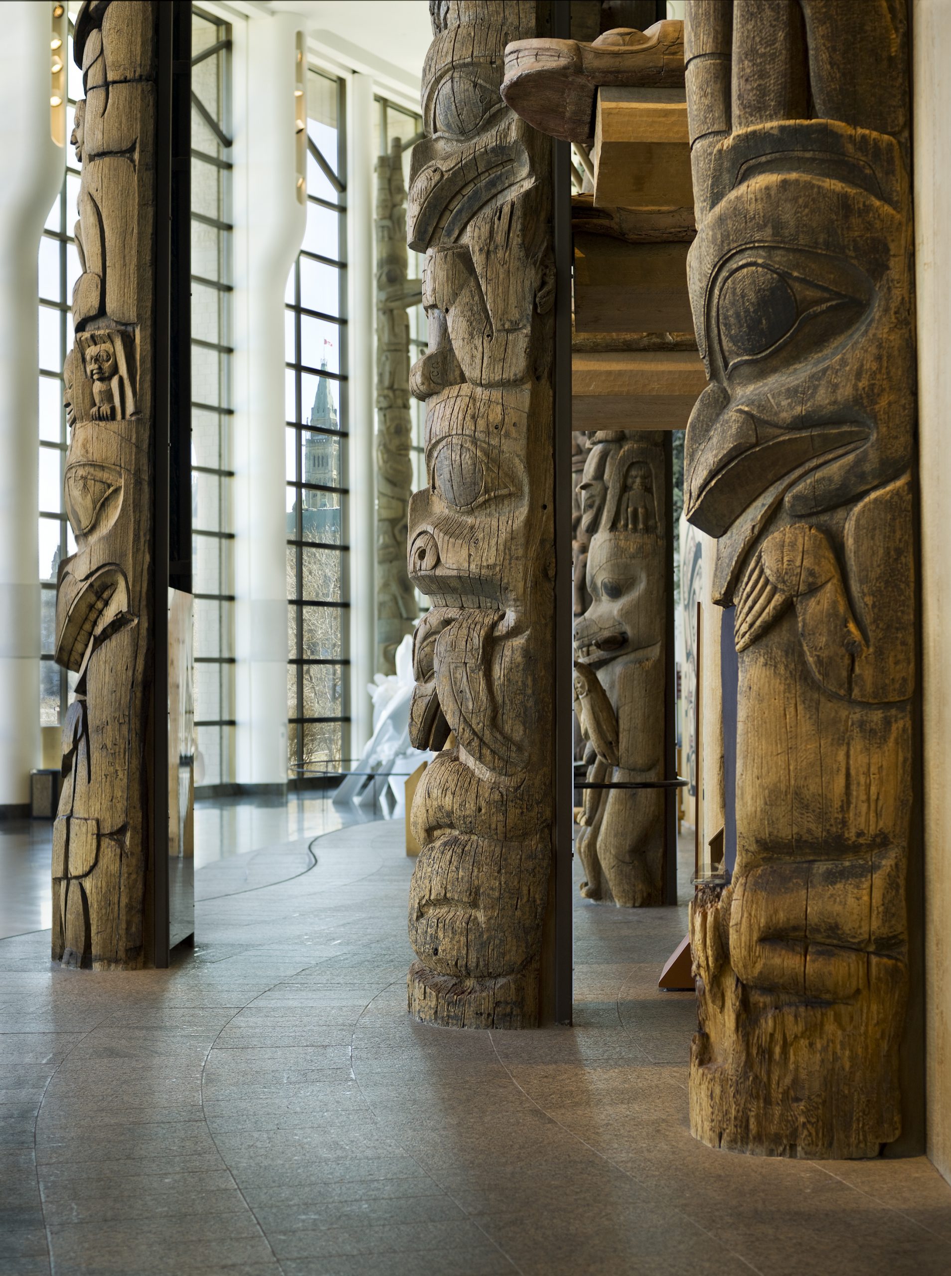 A group of carved totem poles standing in a large glass-walled room.