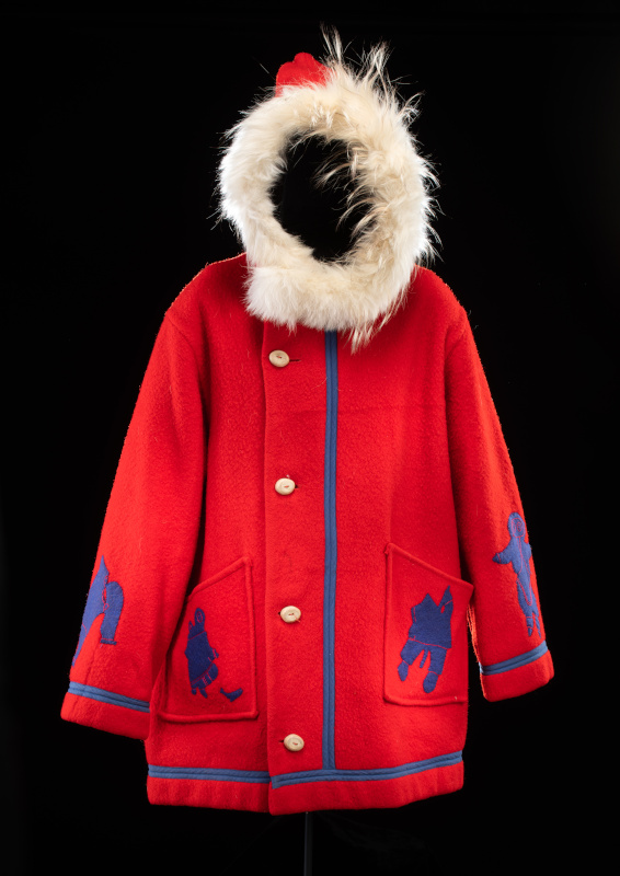 A red cloth parka with blue trim, white fur hood trim, large oval horn buttons, and blue appliqué designs of people and animals on the sleeves and two large front pockets.